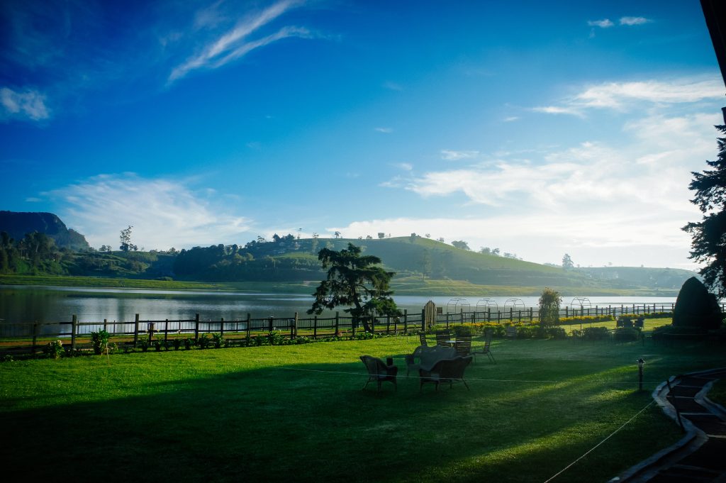 green grass field near body of water under blue sky during daytime in kandy lake