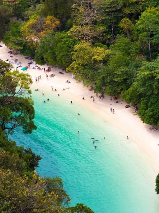 a group of people standing on top of a sandy beach in thailand
