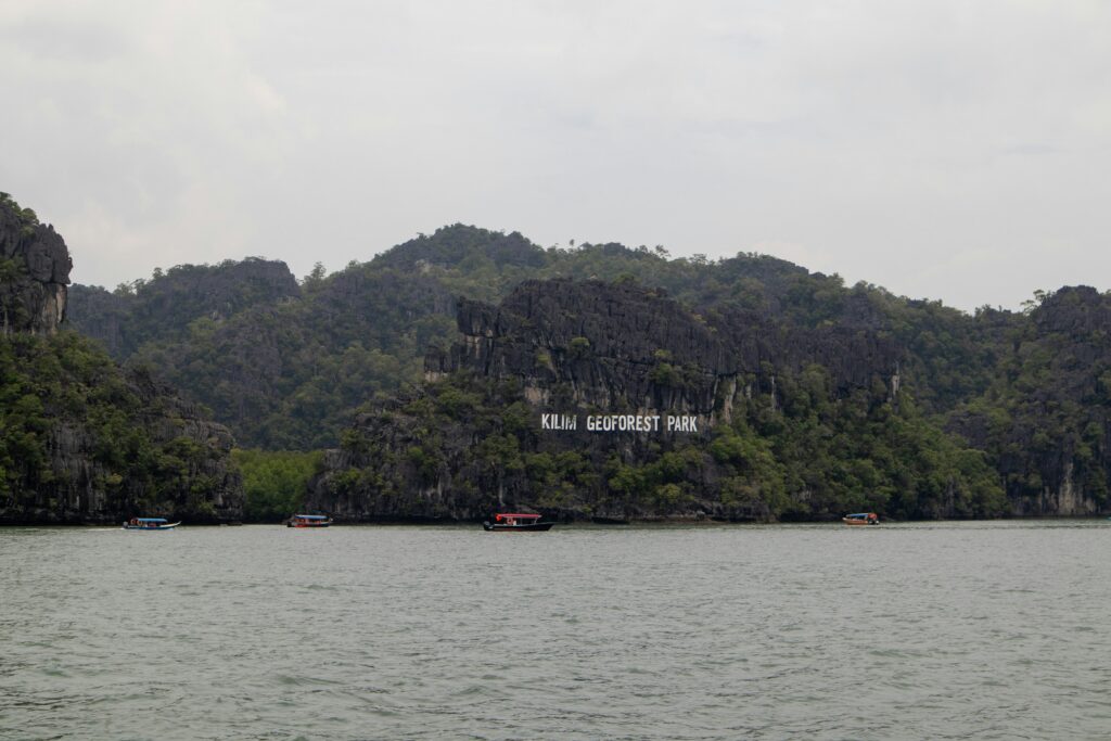 Wooden longtail tour boat cruising along a calm river between towering limestone cliffs in Kilim Geoforest Park