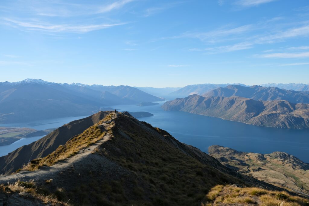 Hiker standing on the grassy ridge of Little Adam's Peak looking out across the dramatic mountain pass of Ella Gap