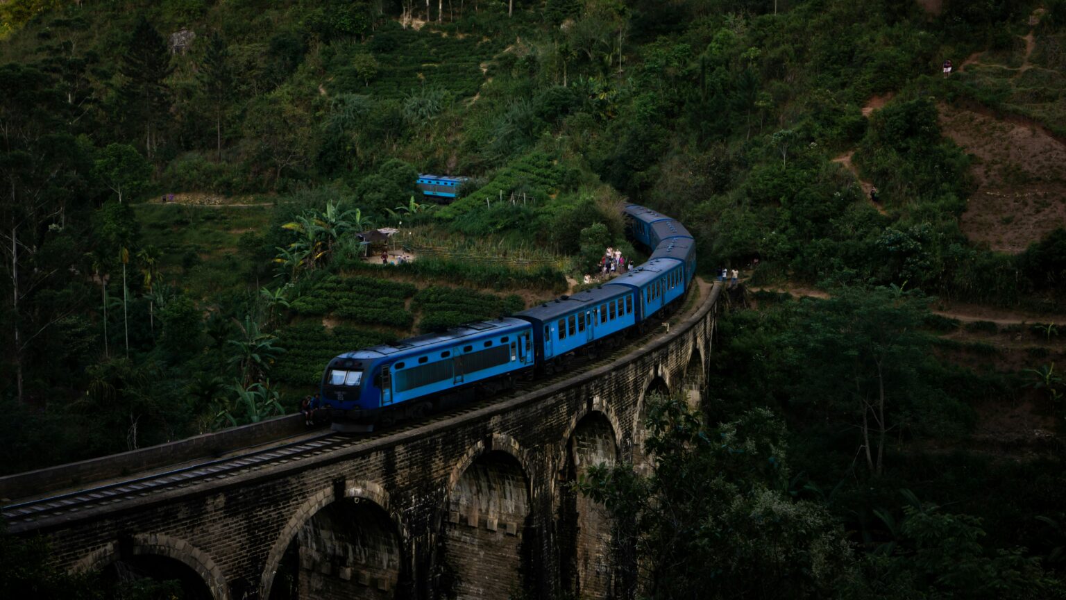 Classic blue passenger train crossing the stone Nine Arch Bridge surrounded by green tea fields in Ella Sri Lanka