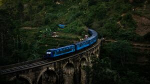 Classic blue passenger train crossing the stone Nine Arch Bridge surrounded by green tea fields in Ella Sri Lanka