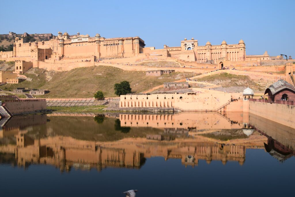 Imposing sandstone walls of Amber Fort reflecting in the calm waters of Maota Lake in Jaipur