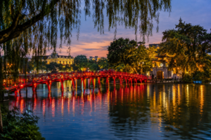Dusk falls over Hoan Kiem Lake and the red Huc Bridge leading to Ngoc Son Temple in Hanoi Old Quarter Vietnam.