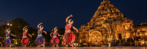 Classical Odissi dancers performing on stage before the illuminated Konark Sun Temple at night.