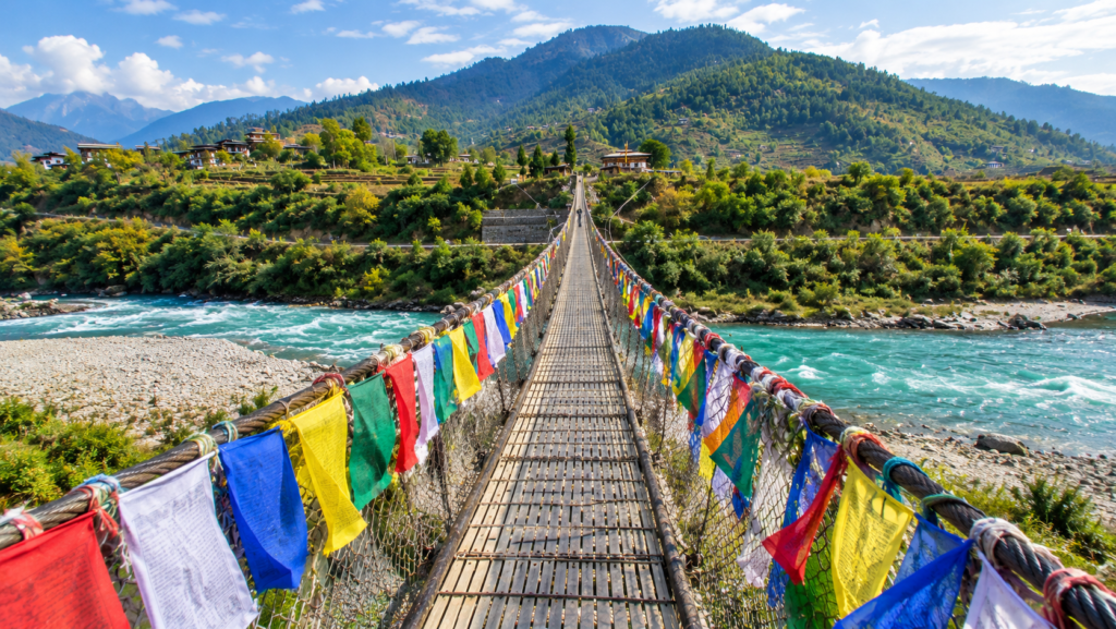 Long suspension bridge adorned with colorful prayer flags spanning the rushing river in Punakha Bhutan.